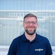 Der Mann trägt ein dunkelblaues Poloshirt mit dem Schriftzug OSMERS KÖSS und lächelt freundlich in die Kamera.