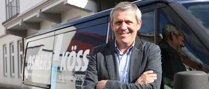 Vor einem Lieferwagen mit dem Logo 'OSMERS KÖSS' steht ein freundlicher Mann, der seine Arme vor der Brust verschränkt.