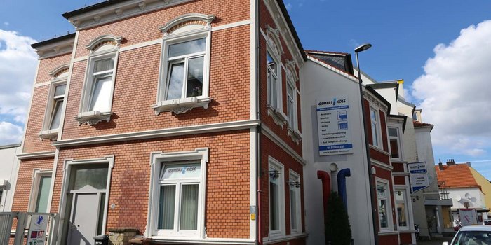 Die Fassade eines charmanten Hauses mit dekorativen Fenstern und einem Schild, das Dienstleistungen im Sanitärbereich anbietet.