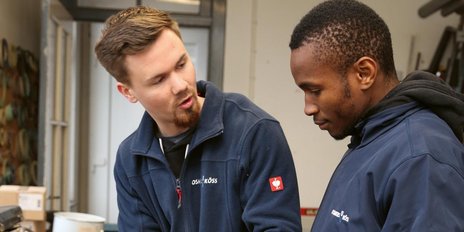 Zwei Männer stehen in einem Raum und diskutieren, während sie auf ein Objekt in ihren Händen schauen.